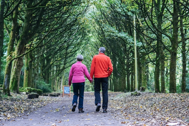 Een ouder paar houdt elkaar vast en loopt in het bos.