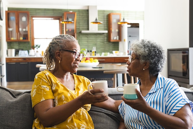 Een oudere Afro-Amerikaanse vrouw en een oudere vrouw van twee rassen praten thuis over koffie.