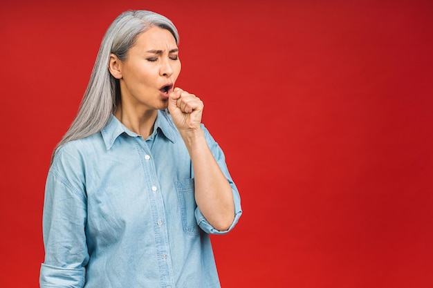 Een oudere aziatische volwassen senior vrouw rimpelde haar gezicht keelpijn gezondheidsproblemen geïsoleerd op rode achtergrond virus concept