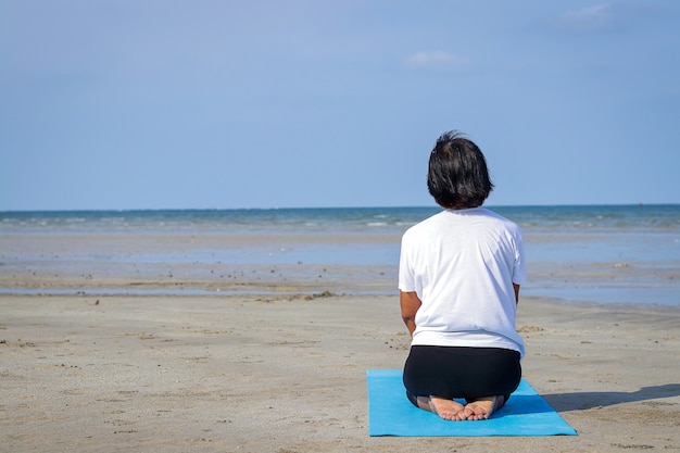 Een oudere Aziatische vrouw speelt 's ochtends alleen yoga aan zee.