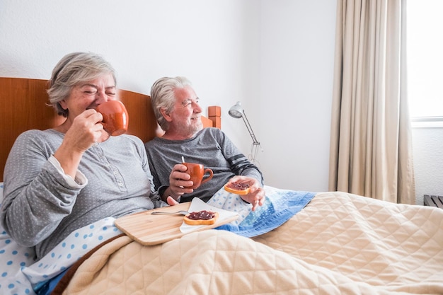 Een oudere echtpaar ontbijt terwijl ze thuis op bed zitten.