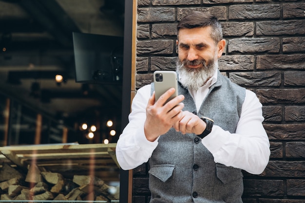 Een oudere grijsharige man met baard gebruikt en praat op een smartphone