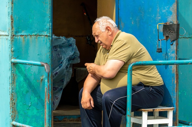 Een oudere grijsharige man zit op een stoel en houdt zijn hand in het gebied van het hart Opa heeft hartproblemen Obesitas en hartpijn op oudere leeftijd