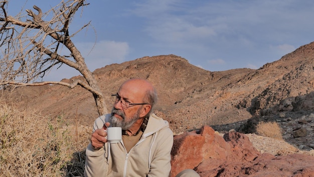 Foto een oudere man drinkt koffie in de woestijn.