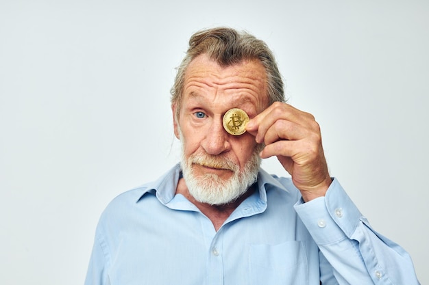 Een oudere man in een blauw shirt bedekt de ogen van een bitcoin-munt