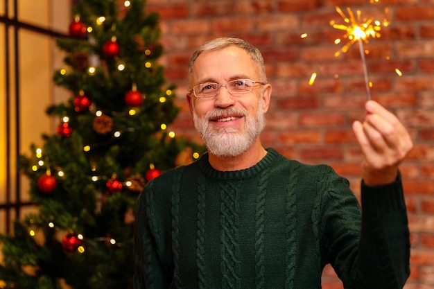 Een oudere man in een groen gebreid met sterretje bij de kerstboom