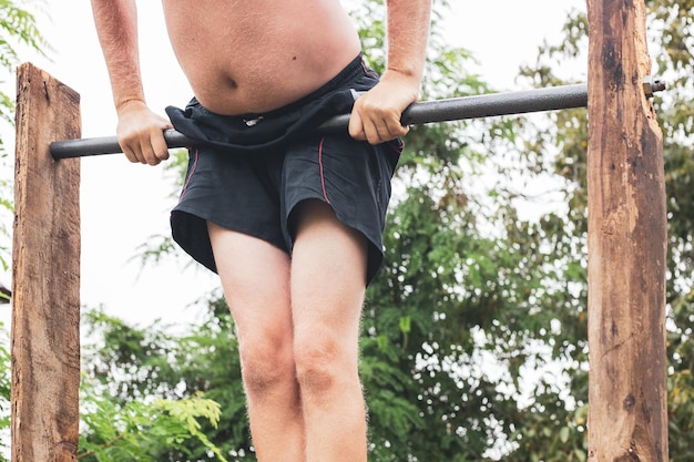 Een oudere man in korte broek en met een buik gaat sporten op de rekstok Actieve levensstijl na pensionering