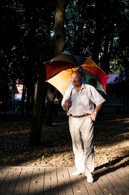 Een oudere man staat onder een grote veelkleurige paraplu Een gepensioneerde op een wandeling in het park