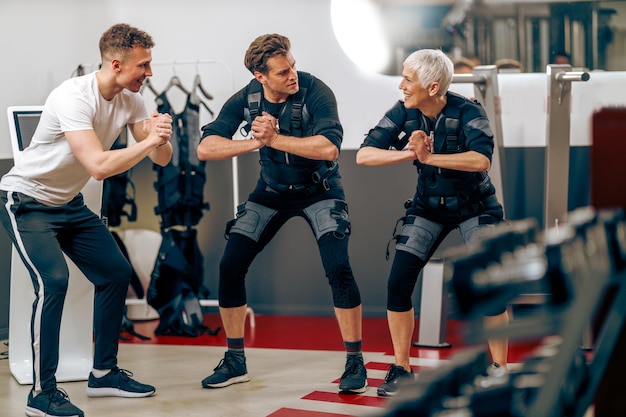 Een oudere moeder en haar zoon van middelbare leeftijd hebben een EMS-workout met personal trainer in de sportschool.