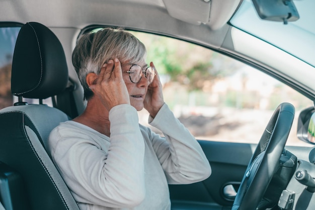 Een oudere of volwassen vrouw die tijdens het rijden erge hoofdpijn heeft en voelt in de auto pijn voelt tijdens het rijden op de weg