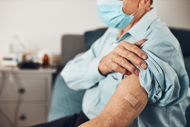 Een oudere patiënt houdt de mouw van zijn shirt omhoog met een pleister op de plaats van de injectie van het vaccin tegen covid-19