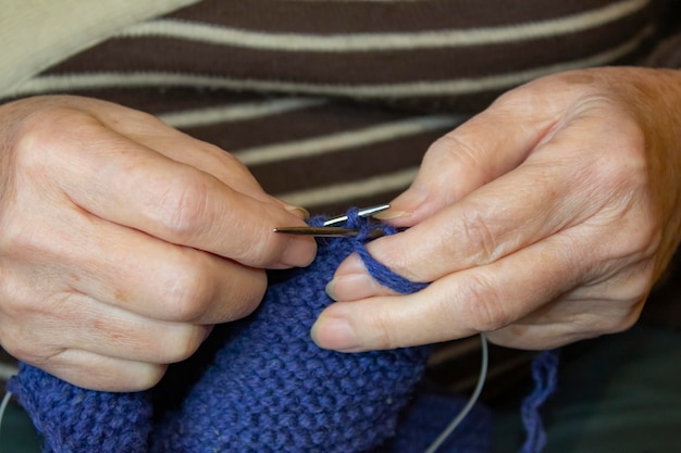 Een oudere vrouw breit op breinaalden met blauwe draden.