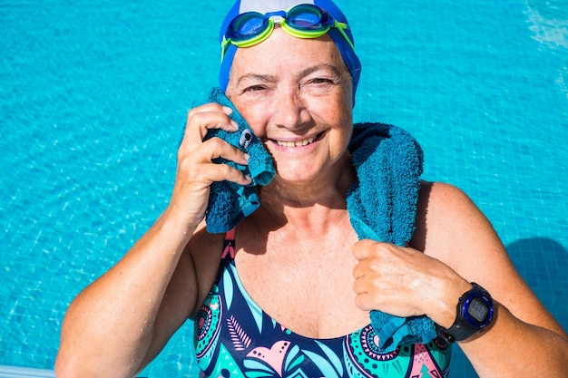 Een oudere vrouw die geniet van het zwembad. Een volk met een grote glimlach. Blauwe badmuts en bril. Gezonde levensstijl door lichamelijke activiteit te doen. Zonnige dag en transparant water