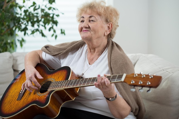 Een oudere vrouw die gitaar speelt op een bank