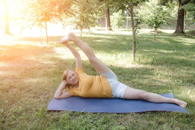 Een oudere vrouw doet yoga in het park en doet complexe rekoefeningen door haar benen op te tillen