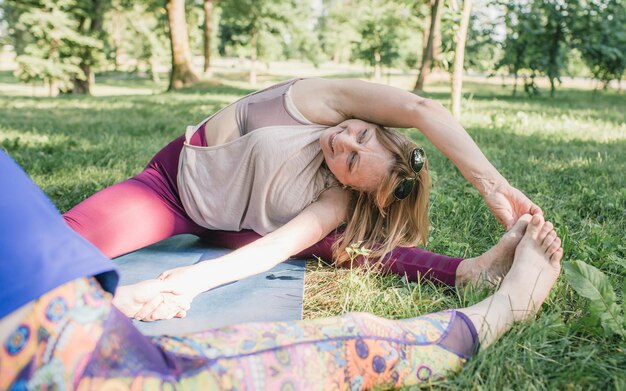 Een oudere vrouw doet yoga in het park op een mat, hij heft zijn benen hoog op en strekt zich uit