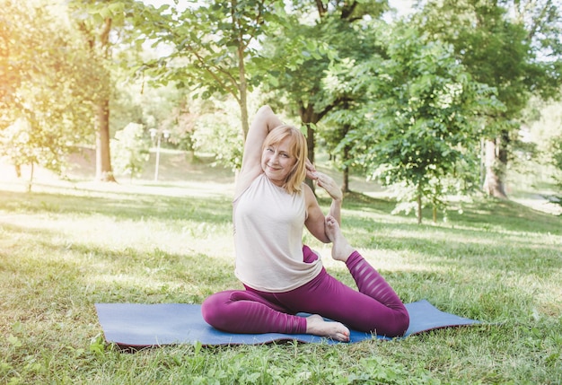 Een oudere vrouw doet yoga in het park op een mat Voert complexe asana-oefeningen uit en leidt een gezond leven