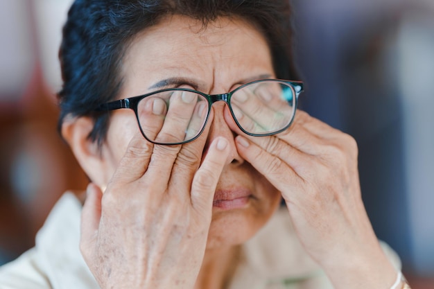 Een oudere vrouw gebruikt haar hand om haar ogen te masseren vanwege vermoeidheid en wazig zicht.