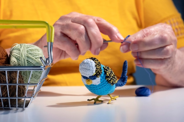 Een oudere vrouw haakt speelgoed. Gebreid vogelspeelgoed op tafel.