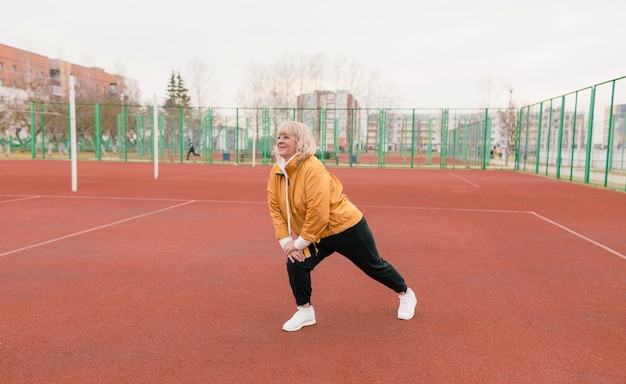 Een oudere vrouw in een geel jasje doet sportoefeningen op een rode loopband. het stadion is een gezonde levensstijl. gepensioneerden en sport. actieve oude vrouw