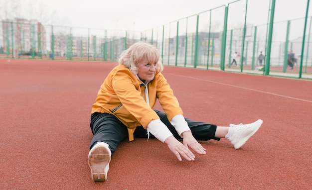 Een oudere vrouw in een geel jasje doet sportoefeningen op een rode loopband. het stadion is een gezonde levensstijl. gepensioneerden en sport. actieve oude vrouw