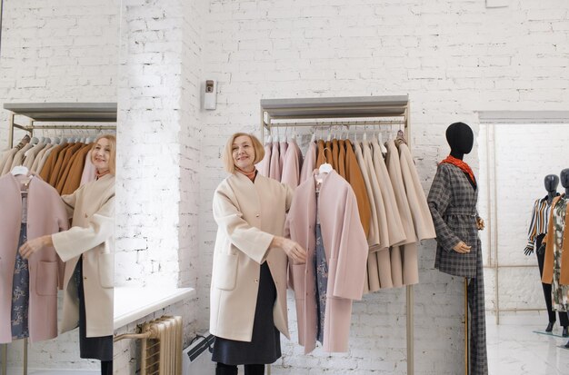 Een oudere vrouw in een kledingwinkel kiest een jas Winkelen kleding kopen