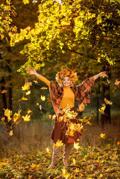 Een oudere vrouw loopt in het herfstbos. Gooit gele bladeren omhoog