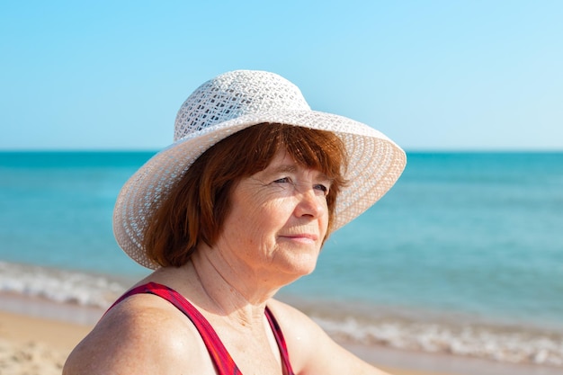 Een oudere vrouw met een hoed aan de kust op een zonnige dag kijkt weg en lacht close Zomertijdverdrijf met pensioen