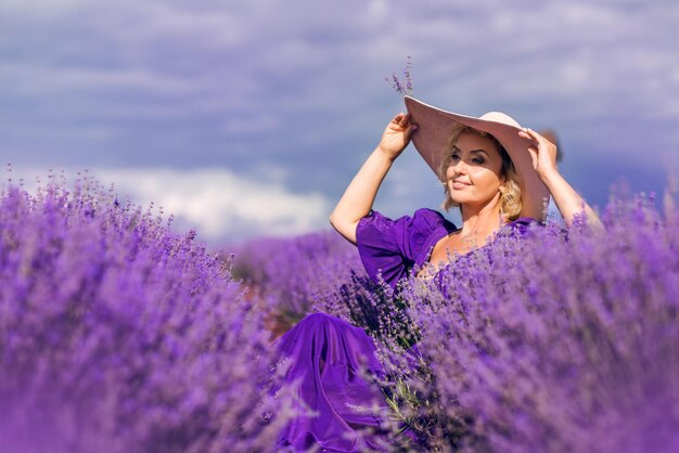 Een oudere vrouw met een hoed zit in een lavendelveld