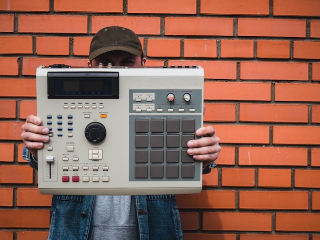 Foto een ouderwetse drummachine uit de jaren 90 in de handen van een beatmaker tegen een bakstenen muur retro digitaal muziekinstrument voor hiphopproducenten en beatmakers