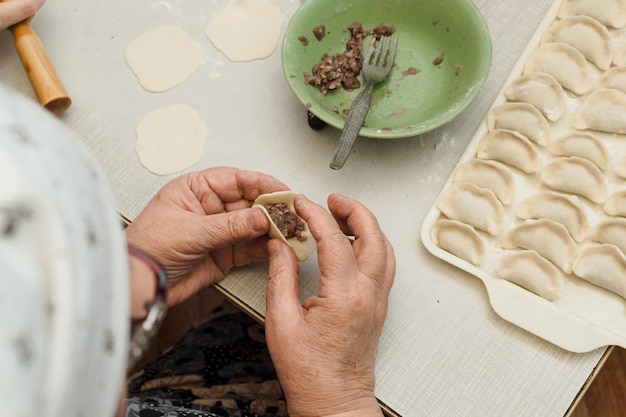 Een over de schouder aanzicht van een oudere vrouw die het deeg verzegelt om een vleesknoedel te vormen