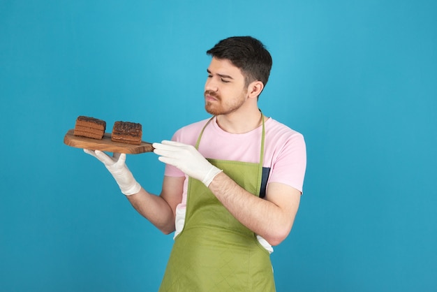 Een overstuur man met verse plakjes cake op blauw.