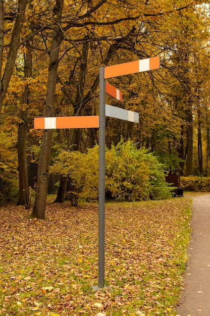 Een paal met richtingaanwijzers in een herfstpark tegen een achtergrond van vergeelde bomen