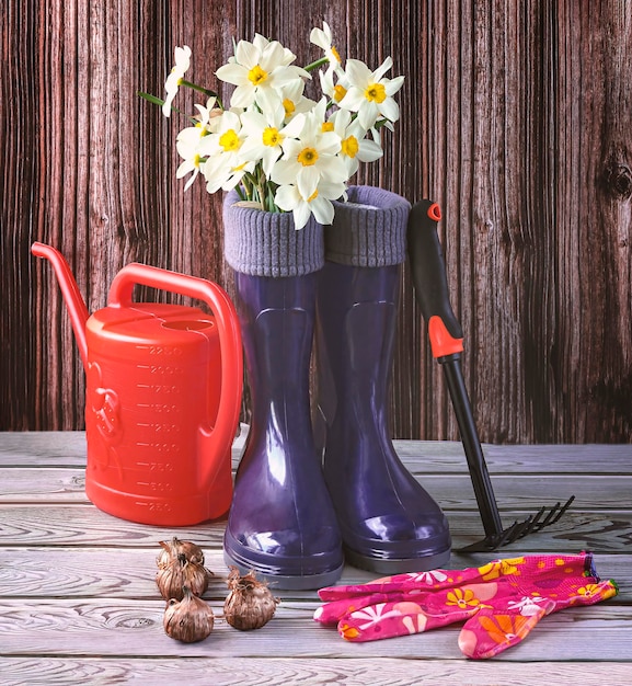 Een paar blauwe rubberen laarzen, een boeket narcisbloemen, zaden en een oranje gieter