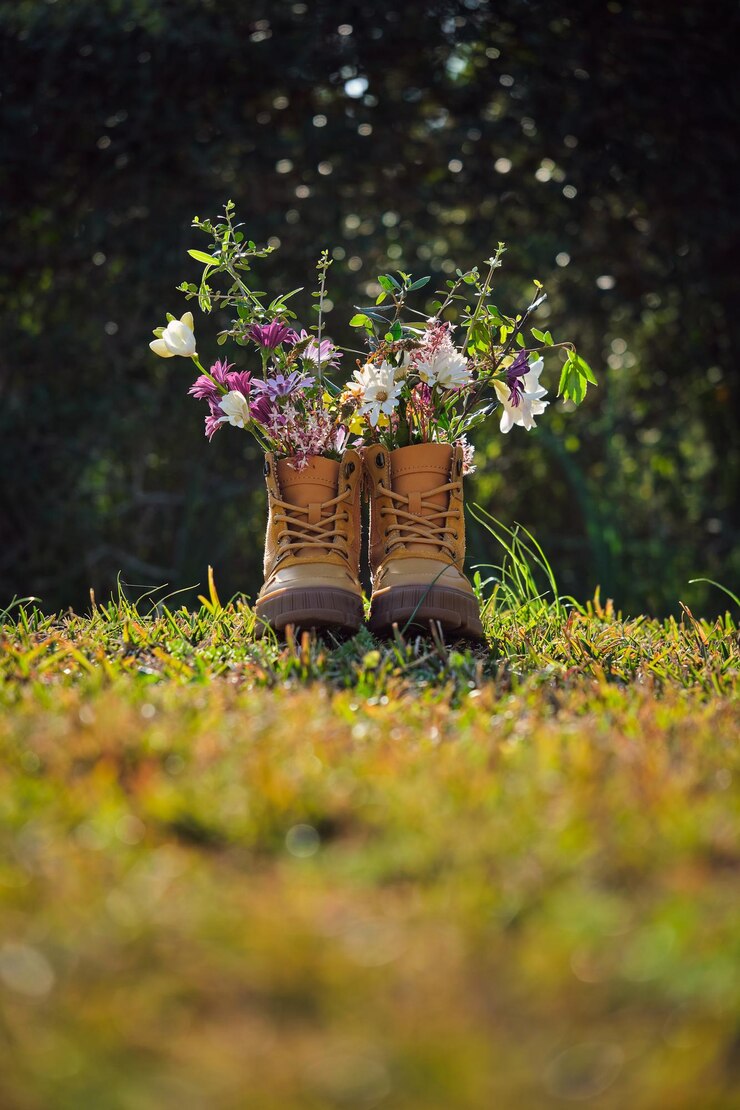 Een paar bruine laarzen met bloeiende kleurrijke bloemen op het gras in de buurt van bomen tijdens een zonnige zomerdag in het voorstedelijk gebied