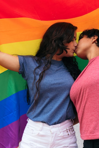 Een paar meisjes zoenen met een gay pride-vlag in de open lucht.