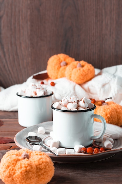 Een paar mokken met cacao en marshmallows, pompoenen en een warme trui op een houten tafel. Verwarmende herfstzoete dranken. Verticale weergave