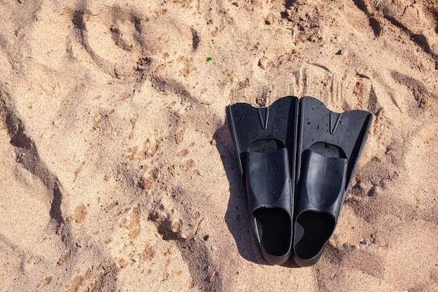 Een paar zwarte flippers op de achtergrond van zand naast het water, bovenaanzicht. Zwemuitrusting