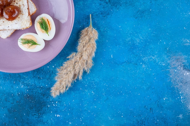 Een paarse plaat van heerlijk wit brood met jam en gekookte eieren op blauw.