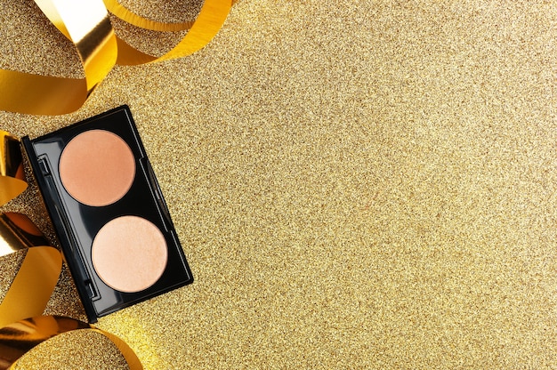 Een palet van beige poeder voor professioneel make-up vrouwelijk gezicht. Een feestelijk cadeau voor een vrouw. Schoonheid trendy cosmetisch product voor perfecte huidskleur op gouden achtergrond met glitter bovenaanzicht. Ruimte kopiëren.