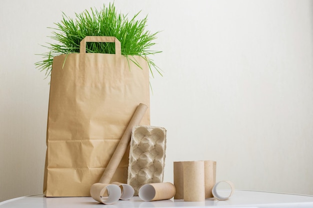 Een papieren zak met groen gras staat op een witte tafel huisvuilrollen gemaakt van karton en p...