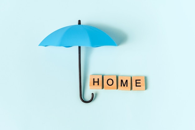 Een paraplu en het opschrift "huis" in houten letters op een blauwe achtergrond. Een symbool van comfort