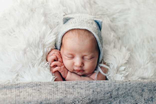 Een pasgeboren baby in een gebreide muts met oren. imitatie van een baby in de baarmoeder. portret van een pasgeborene. het concept van gezondheid, ouderschap, kinderdag, geneeskunde, ivf, mode