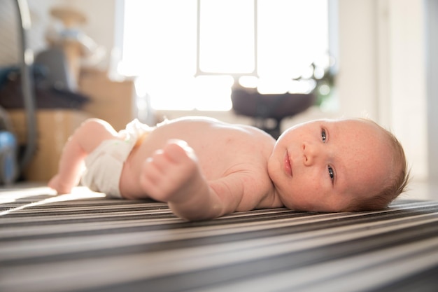 Een pasgeboren baby in een witte luier rusteloos liggend op zijn rug op gestreepte lakens