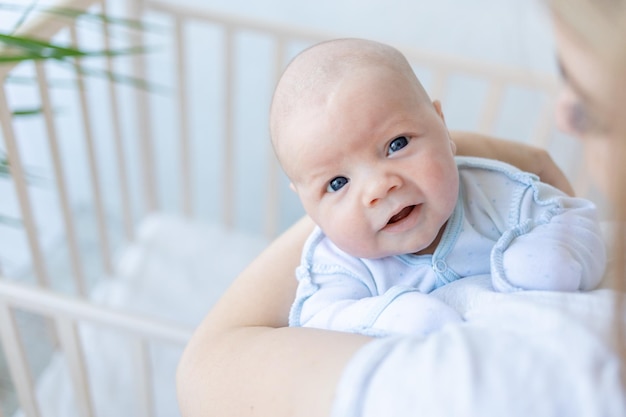 Een pasgeboren babyjongen in de armen van zijn moeder glimlacht bij de wieg thuis ouderlijke liefde en zorg voor de baby in de eerste dagen na de geboorte