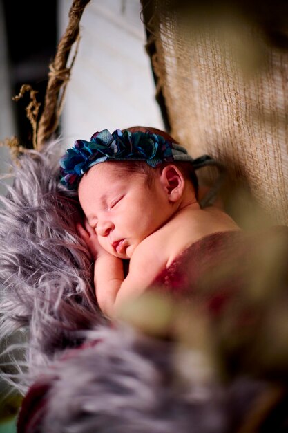 Een pasgeboren babymeisje slaapt op een stoffen strik met een blauwe bloemenhoofdband