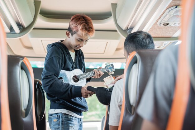 Een passagier geeft geld aan een straatmuzikant die een ukelele draagt terwijl hij in de bus zit