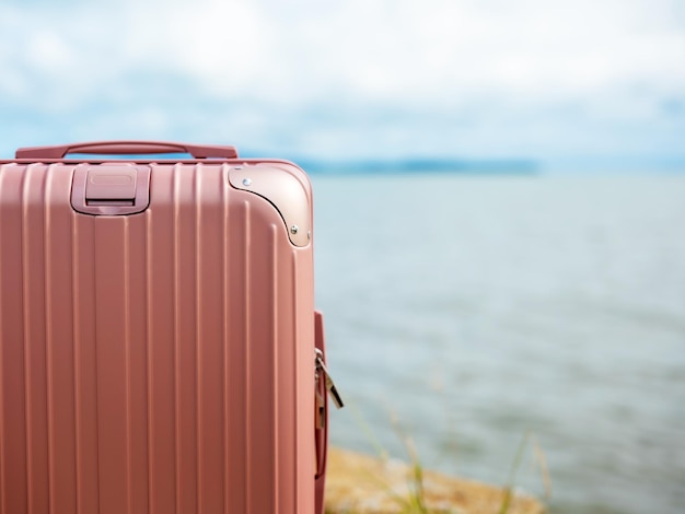 Een pastelroze koffer op de achtergrond is een wazig uitzicht op de zee op een zonnige dag.
