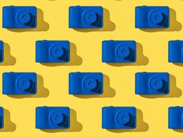 Een patroon van stijlvolle blauwe camera's op een geel oppervlak. Apparatuur voor fotografie.