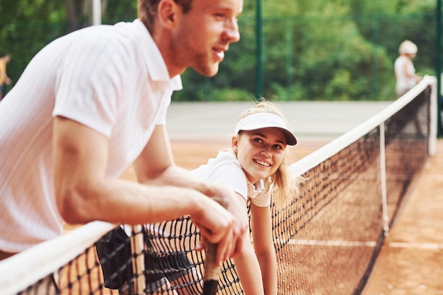 Een pauze nemen door op het net te leunen. Twee mensen in sportuniform spelen samen tennis op het veld.